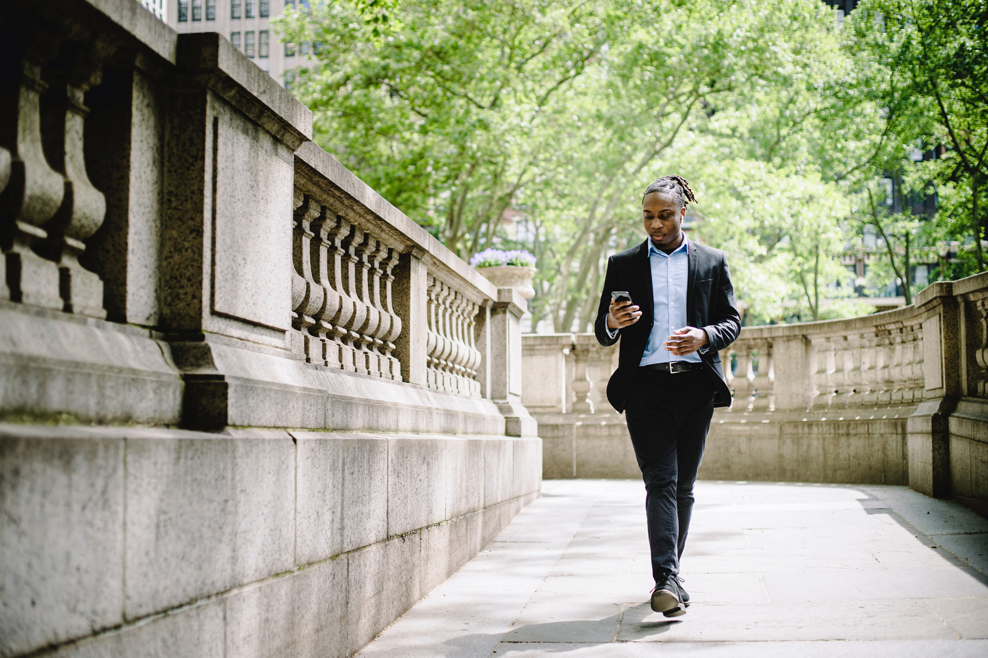 Young African man in casual business clothing walking and checking his smartphone