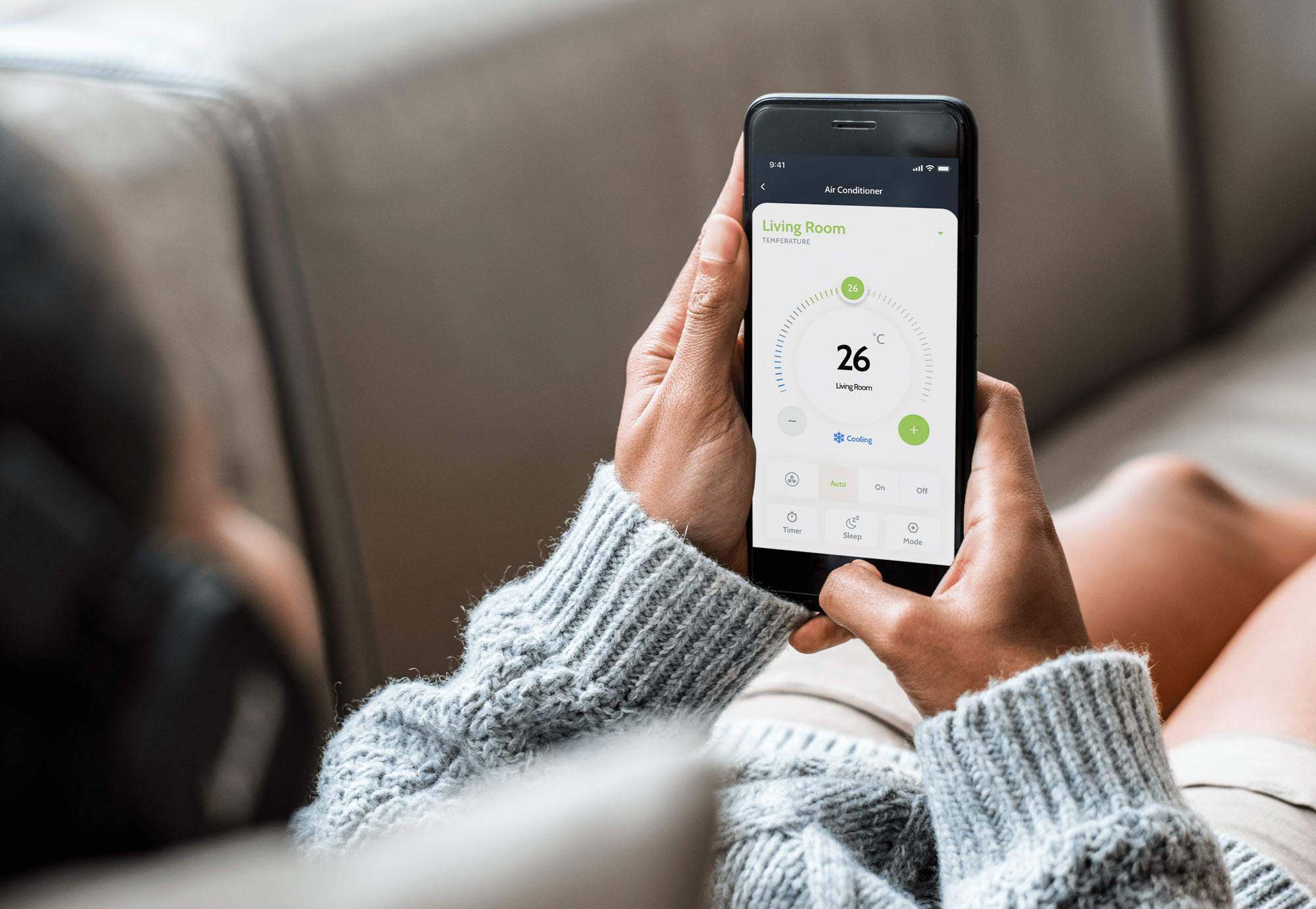 Woman laying down on couch and looking at her smartphone with thermostat screen