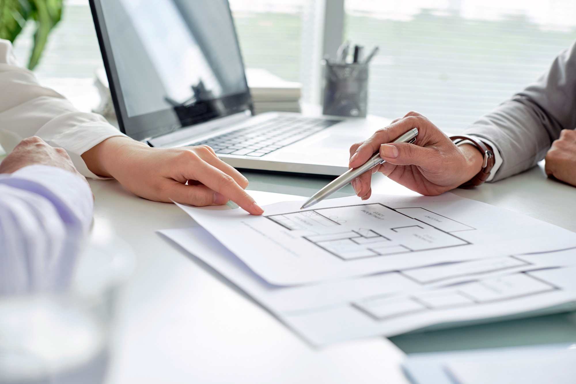 Two peoples hands at desks going over floor plans.