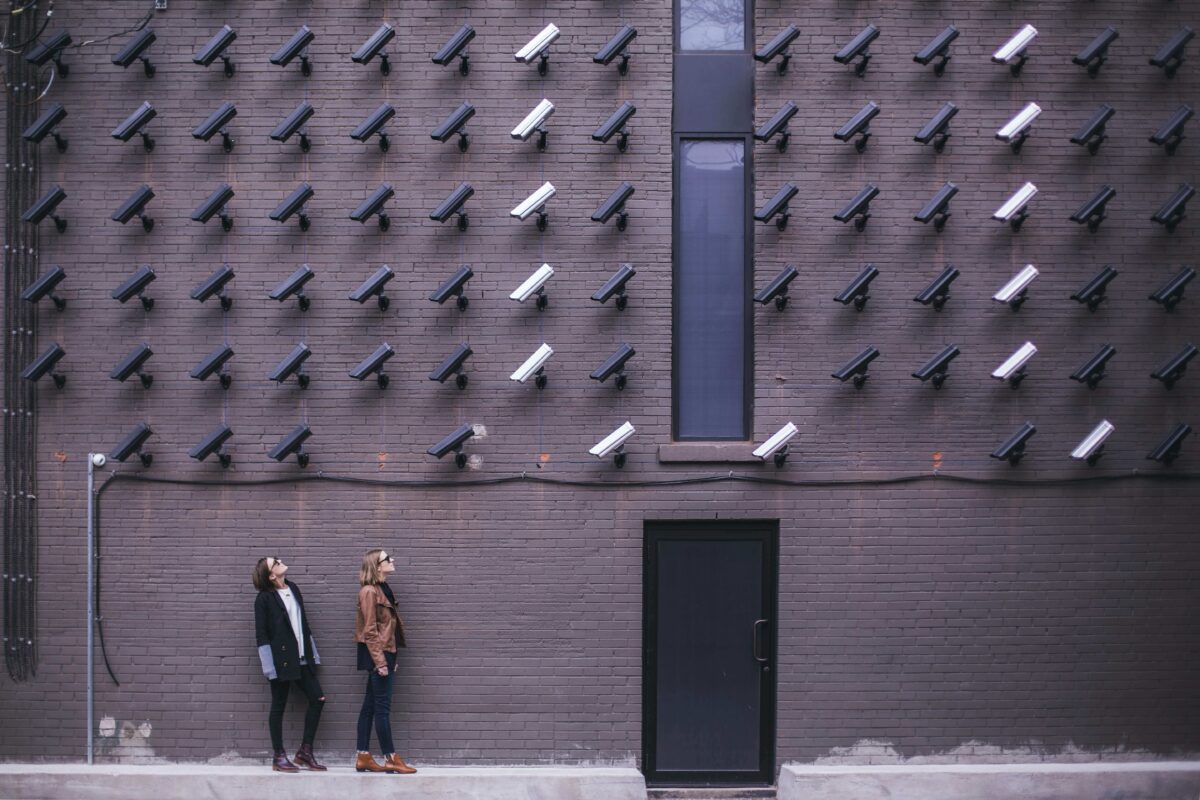 Two people looking up at a brick wall of surveillance cameras